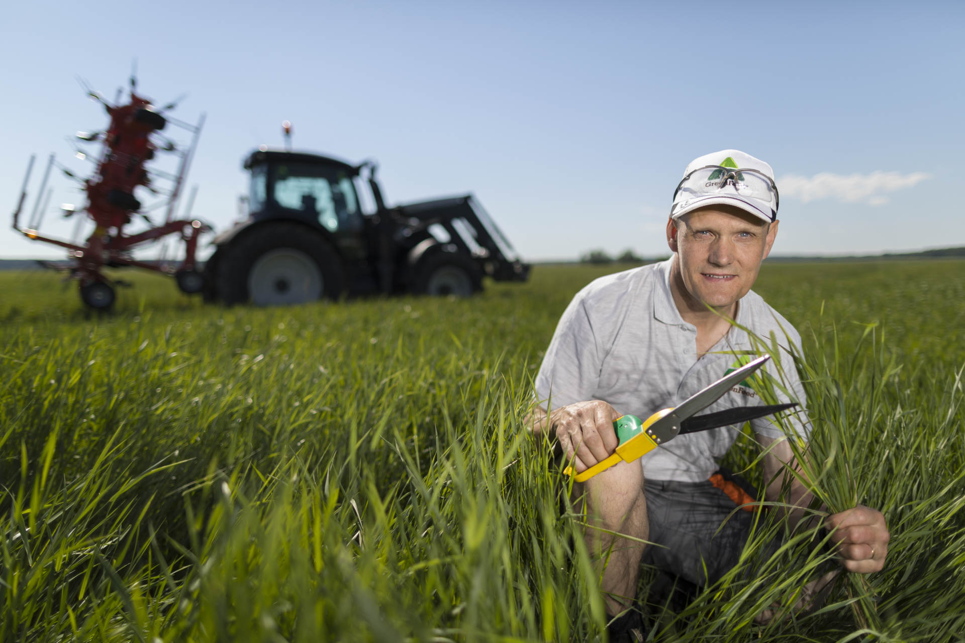 Man mitt i åkern med en traktor i bakgrunden mot en klarblå himmel.